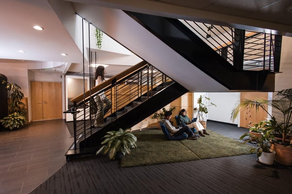 One person walking up a stairwell. Two people working on cushions below the stairs. 