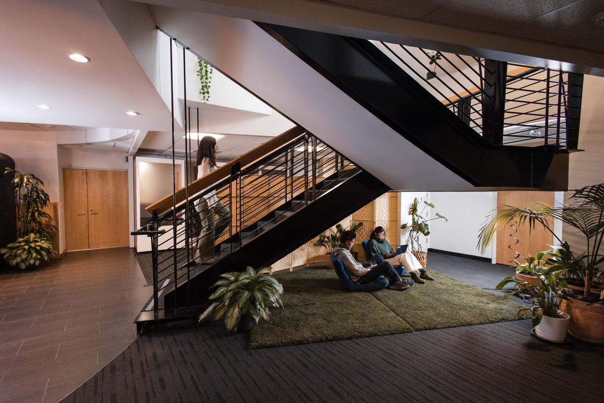 One person walking up a stairwell. Two people working on cushions below the stairs. 